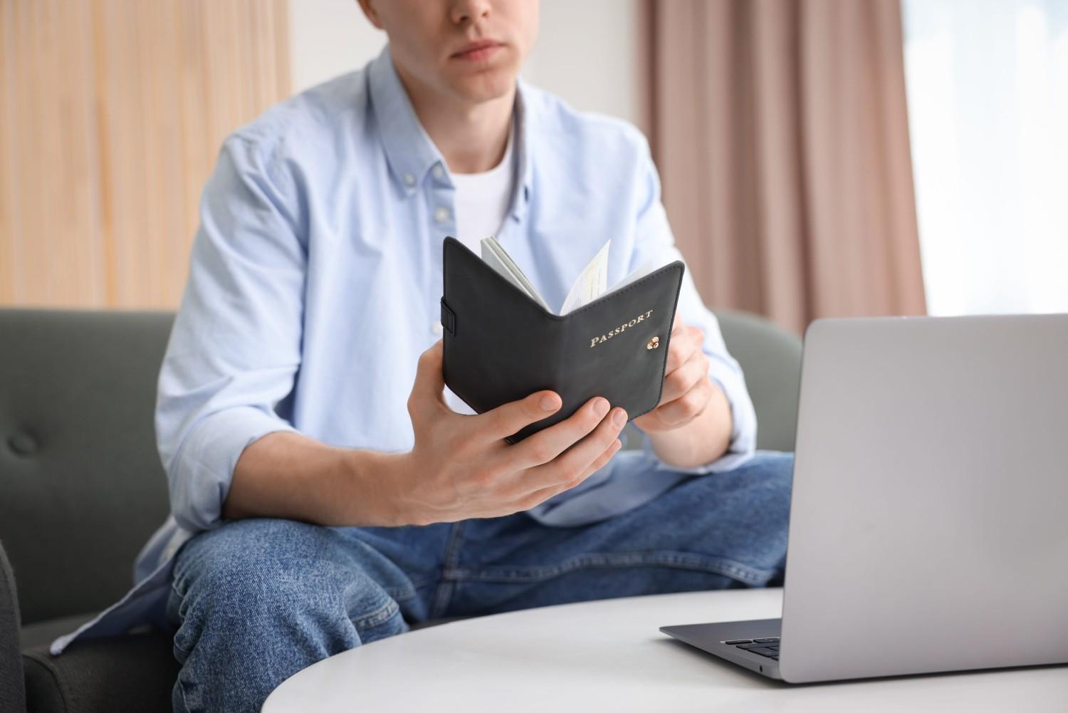 Man With Passport Near Laptop At Home